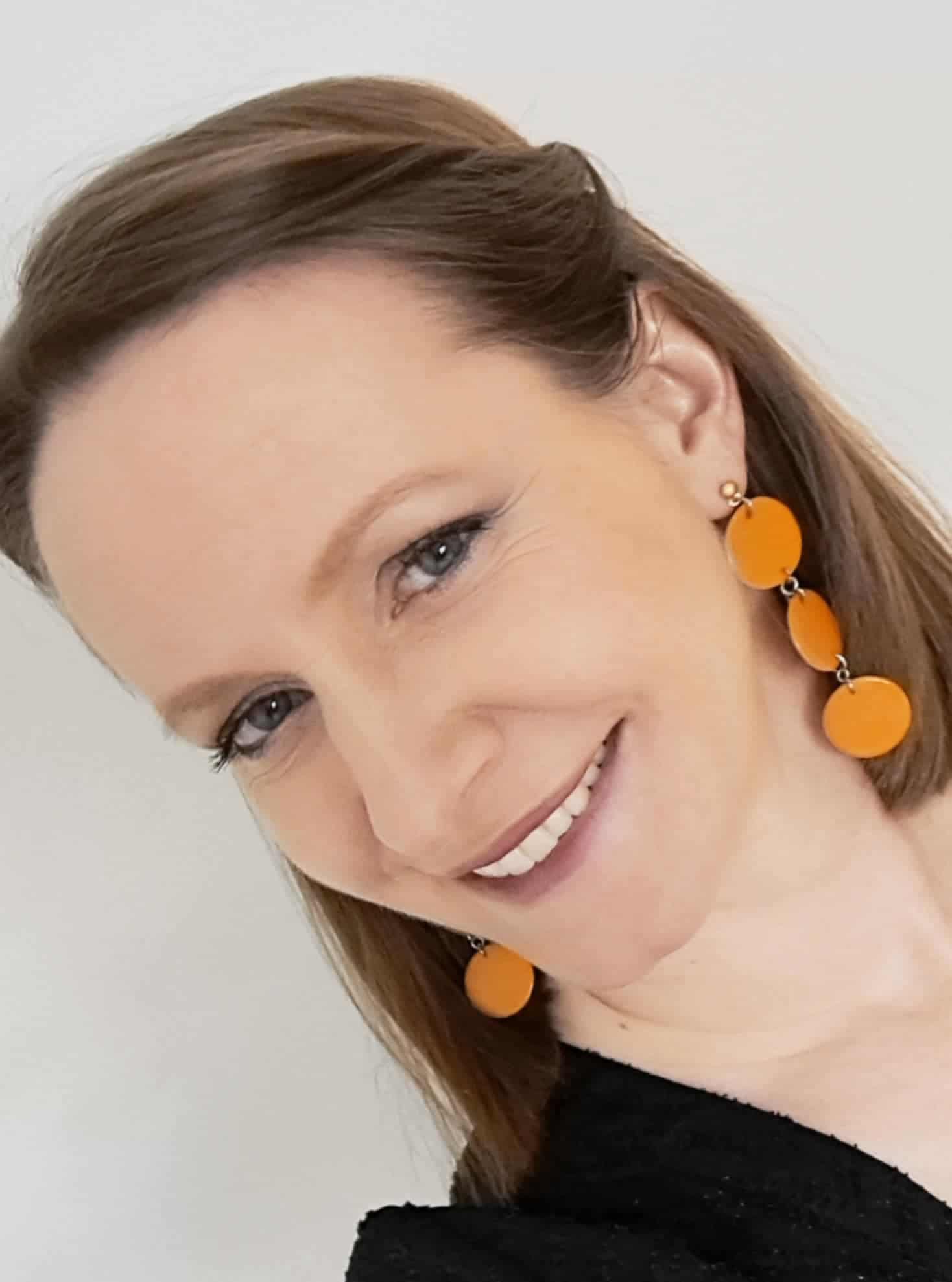 Woman wearing orange earrings with a plain background