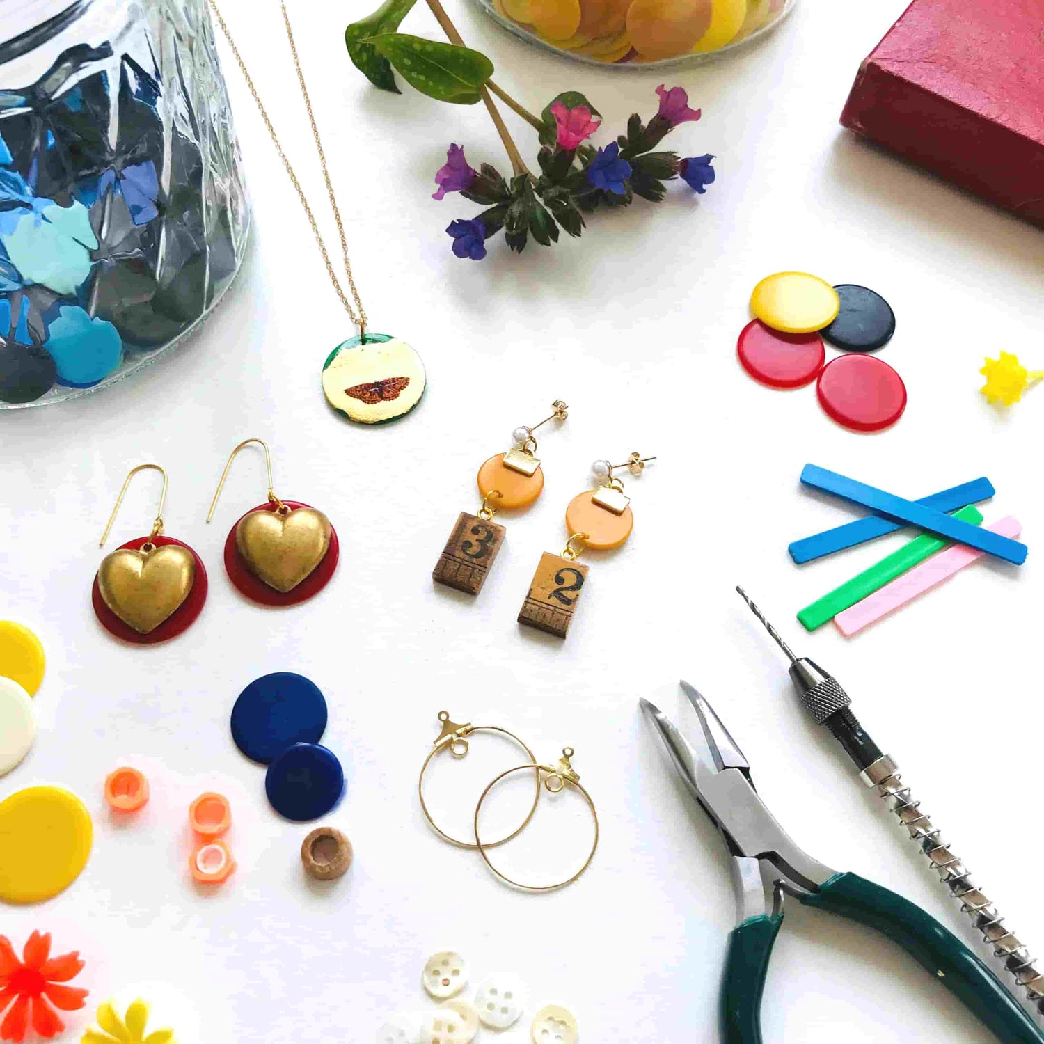 Assorted jewelry-making supplies including earrings, tools, and colorful materials on a white surface.